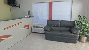A room with a black leather sofa, a small TV on the wall, a window with blinds, and a potted plant. - Kinder Inn (Kinder)