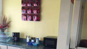A kitchen with a yellow wall, a coffee maker, a microwave, and a trash bin. - Kinder Inn (Kinder)
