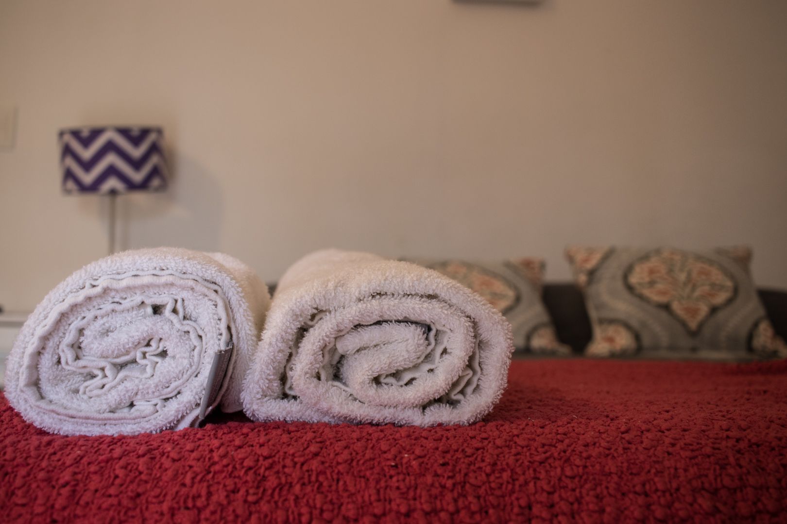 A neatly made bed with rolled towels and a red carpet.