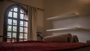 Una habitación con un amplio ventanal de arco, alfombra roja y una toalla sobre la cama.
