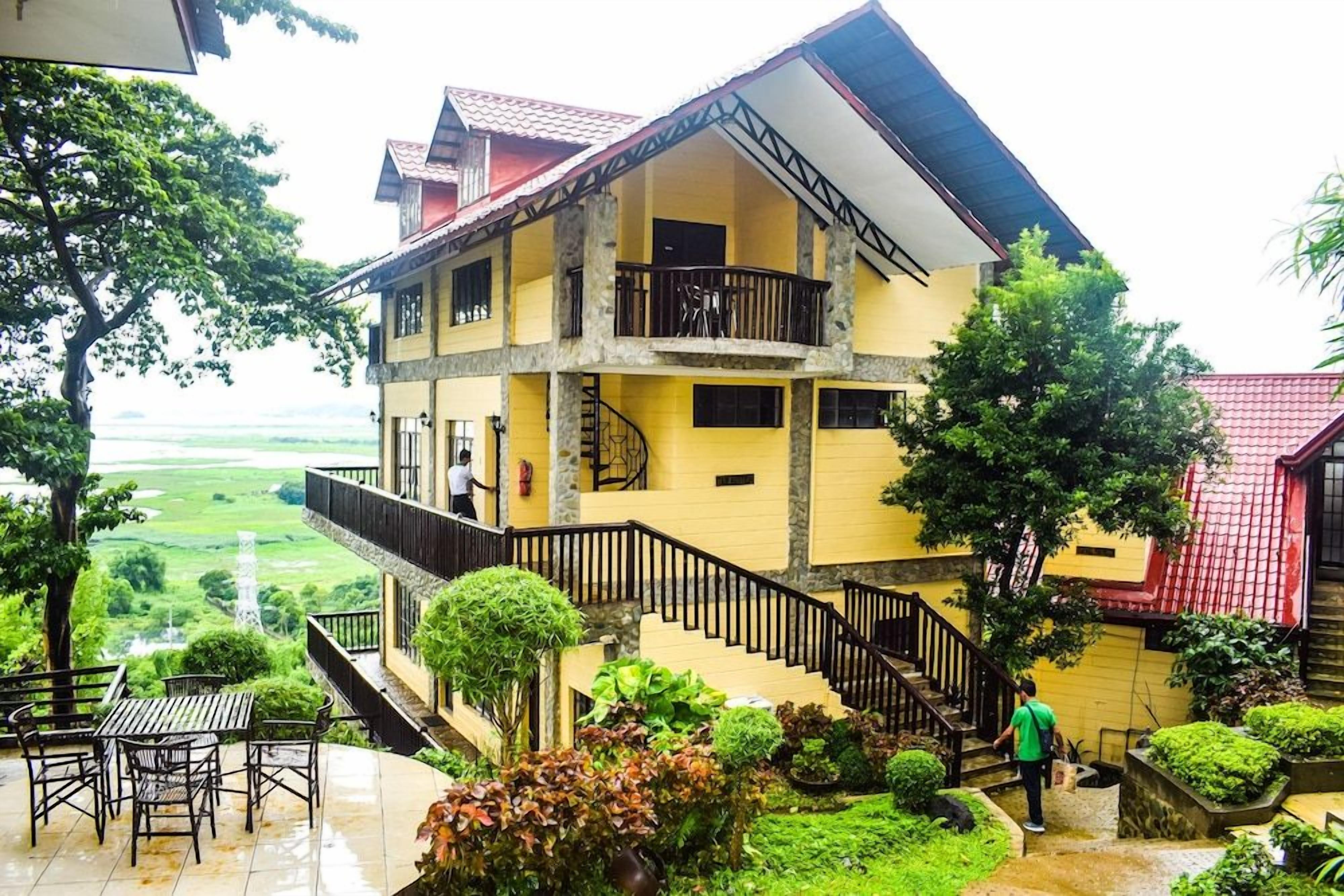 A multi-story building with a balcony, a staircase, and a view of a green landscape.