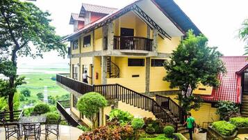 A multi-story building with a balcony, a staircase, and a view of a green landscape.