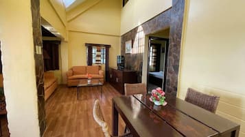 A spacious living area with a wooden dining table, a sofa, and a television.