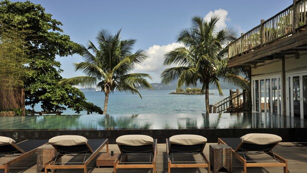 A poolside area with lounge chairs and a view of the sea. - TW Guaimbê Exclusive Suites (Ilhabela)