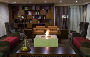 A modern living room with a fireplace, comfortable seating, a bookshelf, and a large window with curtains.