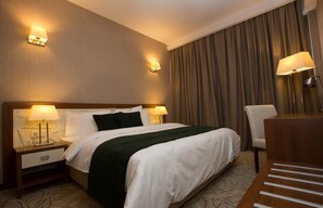 A hotel room with a large bed, two bedside tables with lamps, a chair, and a desk with a lamp.