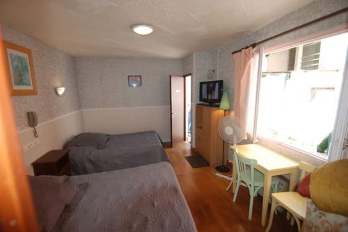 A room with two beds, a desk with a chair, a television, and a window with curtains.