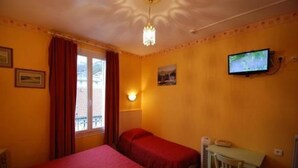 Una habitación con dos camas individuales, un escritorio con silla, televisión y ventana con cortinas.