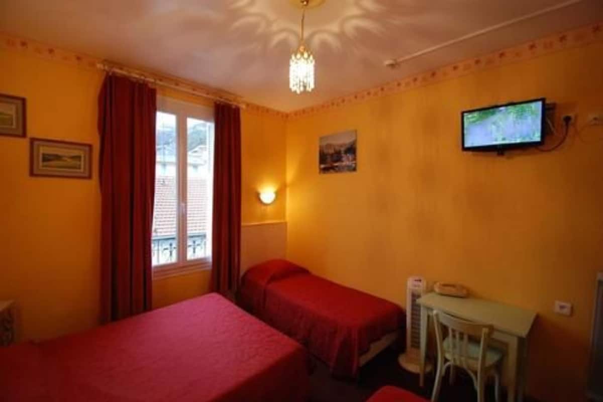 A room with two single beds, a desk with a chair, a television, and a window with curtains.
