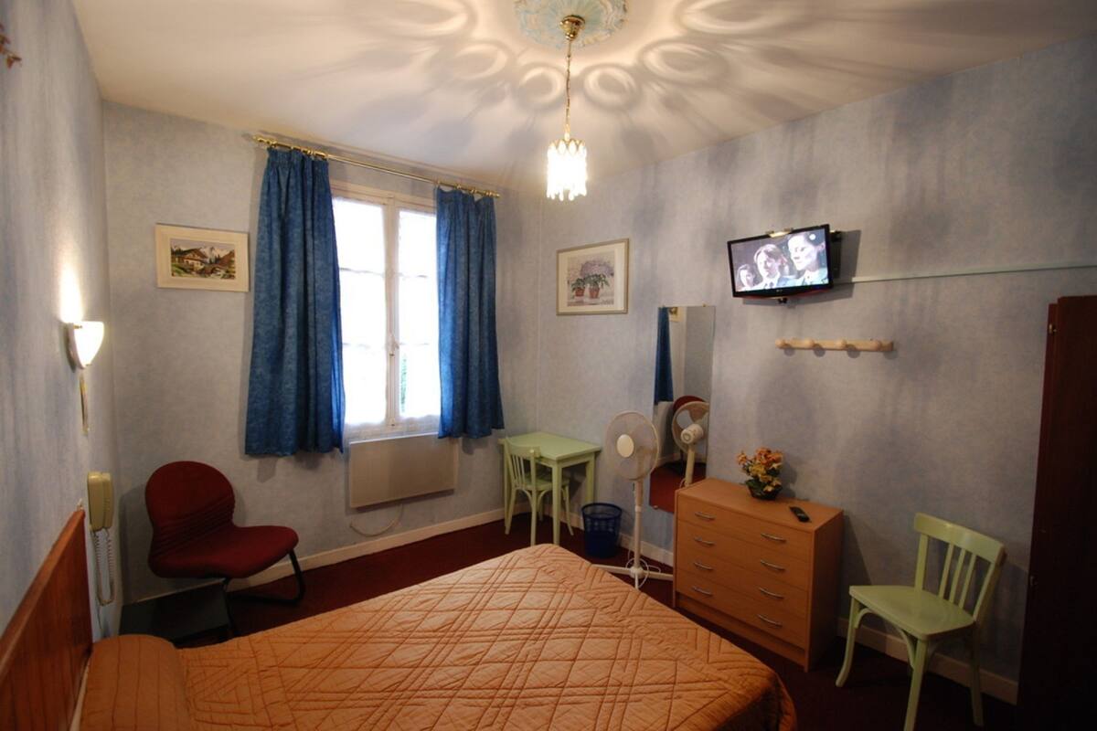 A hotel room with a bed, a desk, a chair, a dresser, a television, and a window with curtains.