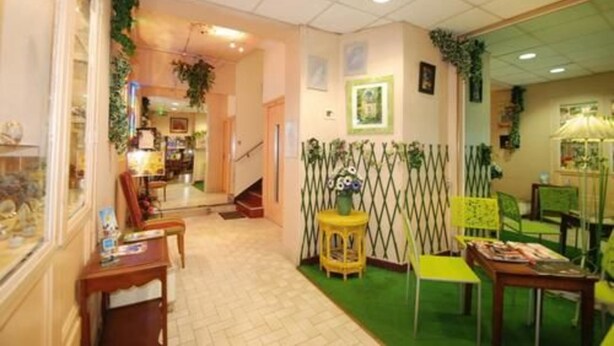 Un vestíbulo de hotel con una escalera, una recepción y una zona alfombrada de color verde.