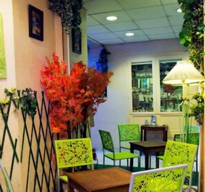 A restaurant interior with a table and chairs, a window with a view, and decorative plants. - Hotel Notre Dame Auxiliatrice (Lourdes)