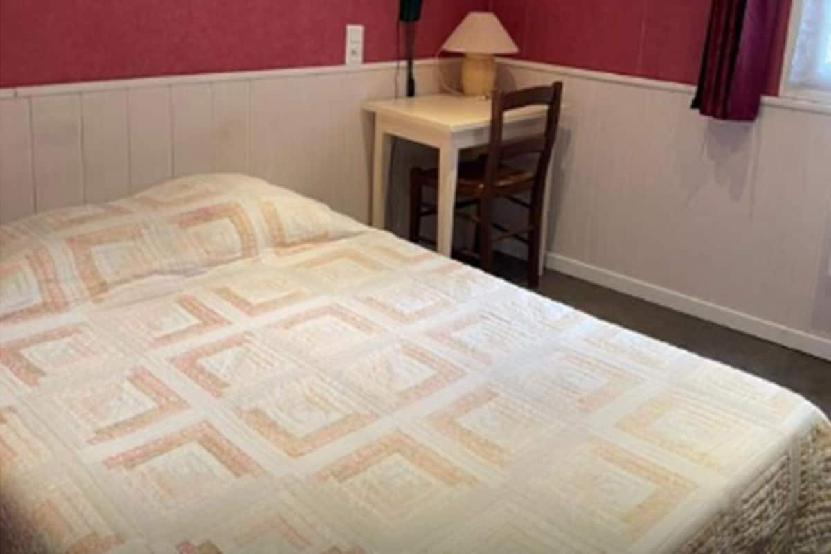 A single bed with a patterned bedspread, a small table with a lamp, and a chair in a room with red walls and white trim.