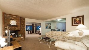 A living room with a fireplace, a sofa, a coffee table, and a dining area in the background. - Sun Lakes By Signature Vacation Rentals (Chandler)