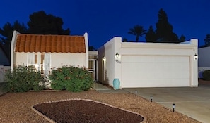 A two-story house with a garage, a well-maintained garden, and a clear sky at dusk.