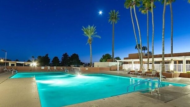 A swimming pool with a clear blue water, surrounded by palm trees and a building with a white fence. - Sun Lakes By Signature Vacation Rentals (Chandler)