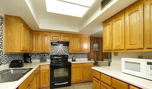 A kitchen with wooden cabinets, a black stove, a white microwave, and a tiled backsplash.