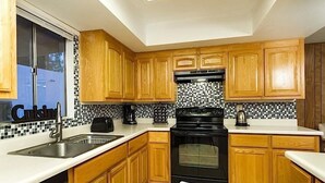 A kitchen with wooden cabinets, a black stove, a sink, and a tiled backsplash. - Sun Lakes By Signature Vacation Rentals (Chandler)