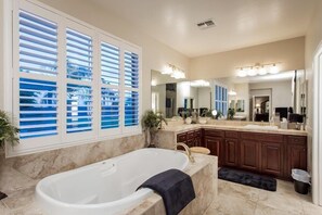 A modern bathroom with a freestanding bathtub, a large vanity with a mirror, and a window with blinds. - The Sound Of Freedom By Signature Vacation Rentals (Surprise)