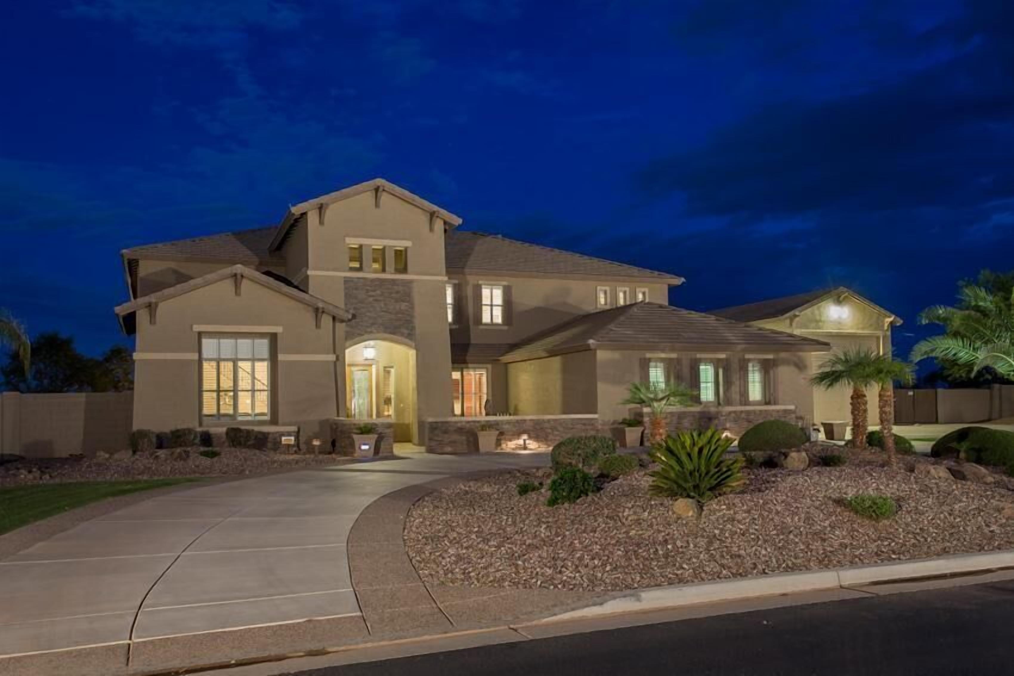 A two-story house with a driveway, a well-maintained lawn, and a landscaped area with shrubs and a small palm tree.