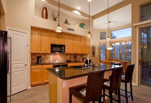 A spacious kitchen with wooden cabinets, a central island with bar stools, and pendant lighting.
