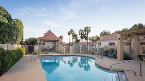 A swimming pool with a tiled deck, surrounded by palm trees and a building with a red roof. - Take It Easy By Signature Vacation Rentals (Tempe)