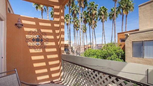 A balcony with a lattice railing, a decorative wall piece, and tall palm trees in the background. - Sweet Escape By Signature Vacation Rentals (Scottsdale)