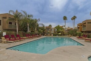 A swimming pool with red lounge chairs and palm trees. - Sweet Escape By Signature Vacation Rentals (Scottsdale)