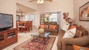 A living room with a TV, wooden furniture, a ceiling fan, and a large window. - Sweet Escape By Signature Vacation Rentals (Scottsdale)
