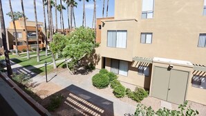 A modern building with a flat roof, multiple windows, and a small garden area with palm trees and shrubs. - Sweet Escape By Signature Vacation Rentals (Scottsdale)