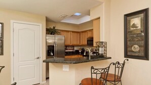 A compact kitchen with a central island, wooden cabinets, and a refrigerator. - Sunny Sky Condo By Signature Vacation Rentals (Peoria)