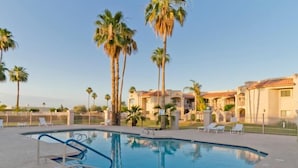 A swimming pool with palm trees and lounge chairs, surrounded by a fenced area with buildings in the background. - Sunny Sky Condo By Signature Vacation Rentals (Peoria)