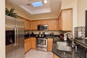 A modern kitchen with stainless steel appliances, wooden cabinets, a skylight, and a granite countertop.