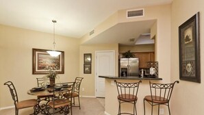 A dining area with a round table, four chairs, a chandelier, and a kitchen in the background. - Sunny Sky Condo By Signature Vacation Rentals (Peoria)