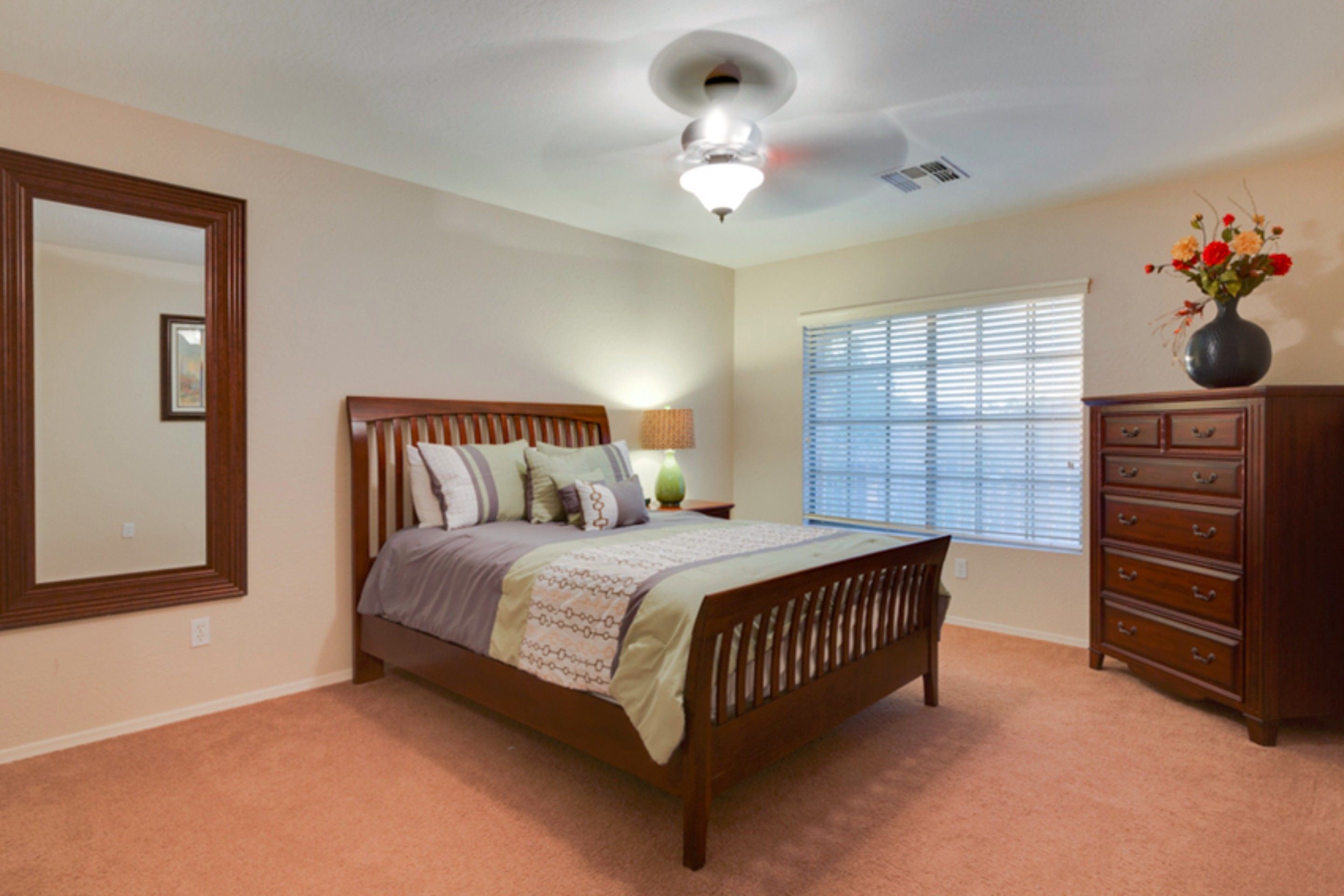 A bedroom with a wooden bed, a dresser, a mirror, and a window with blinds.