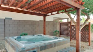 Una vasca idromassaggio sotto un gazebo in legno, con un muro di mattoni e un recinto di legno sullo sfondo.