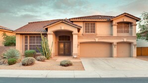 Una casa a due piani con un garage, un ingresso principale con una porta e un piccolo giardino antistante con aiuole.