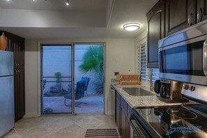 A modern kitchen with a sliding glass door leading to an outdoor patio, a built-in oven, and a coffee maker. - Southwest Sanctuary By Signature Vacation Rentals (Scottsdale)