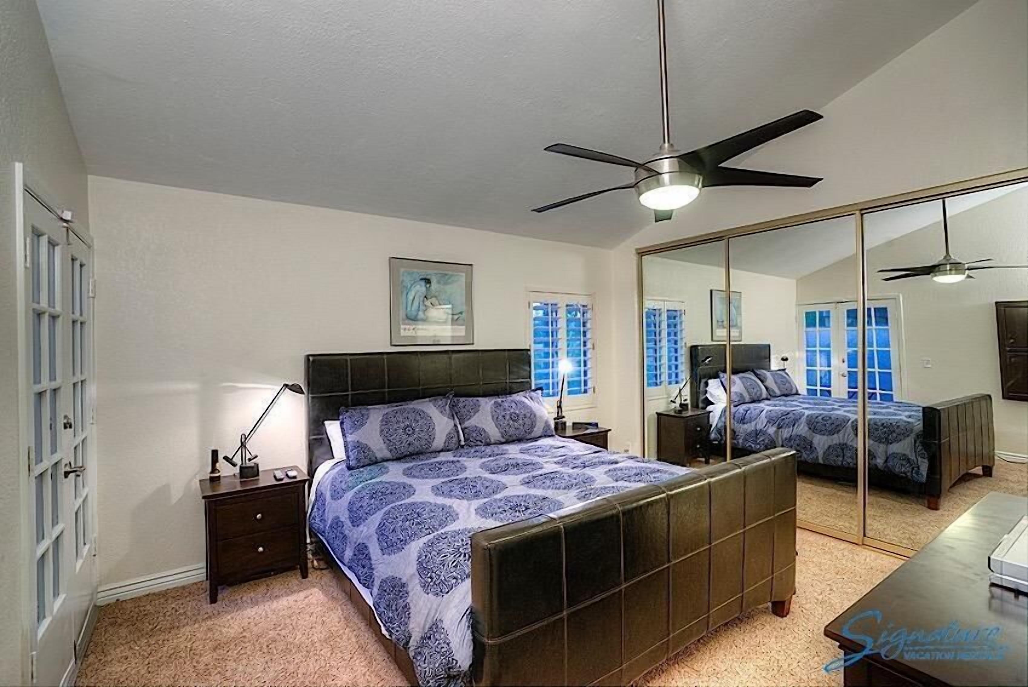 A bedroom with a large bed, a ceiling fan, a nightstand, a dresser, and a mirror.