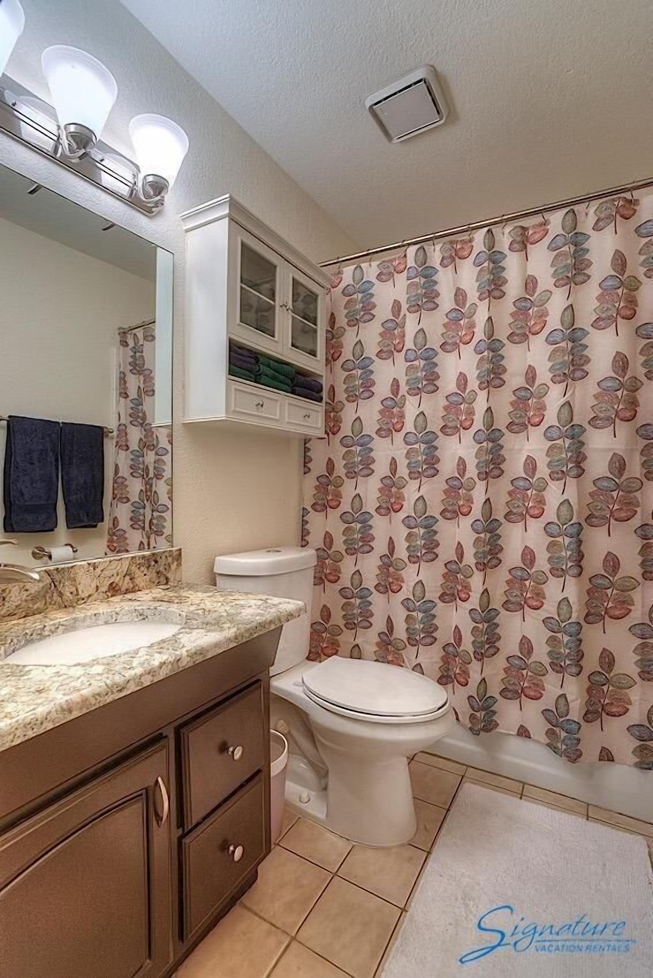 A bathroom with a marble sink, a toilet, and a shower curtain with a leaf pattern.