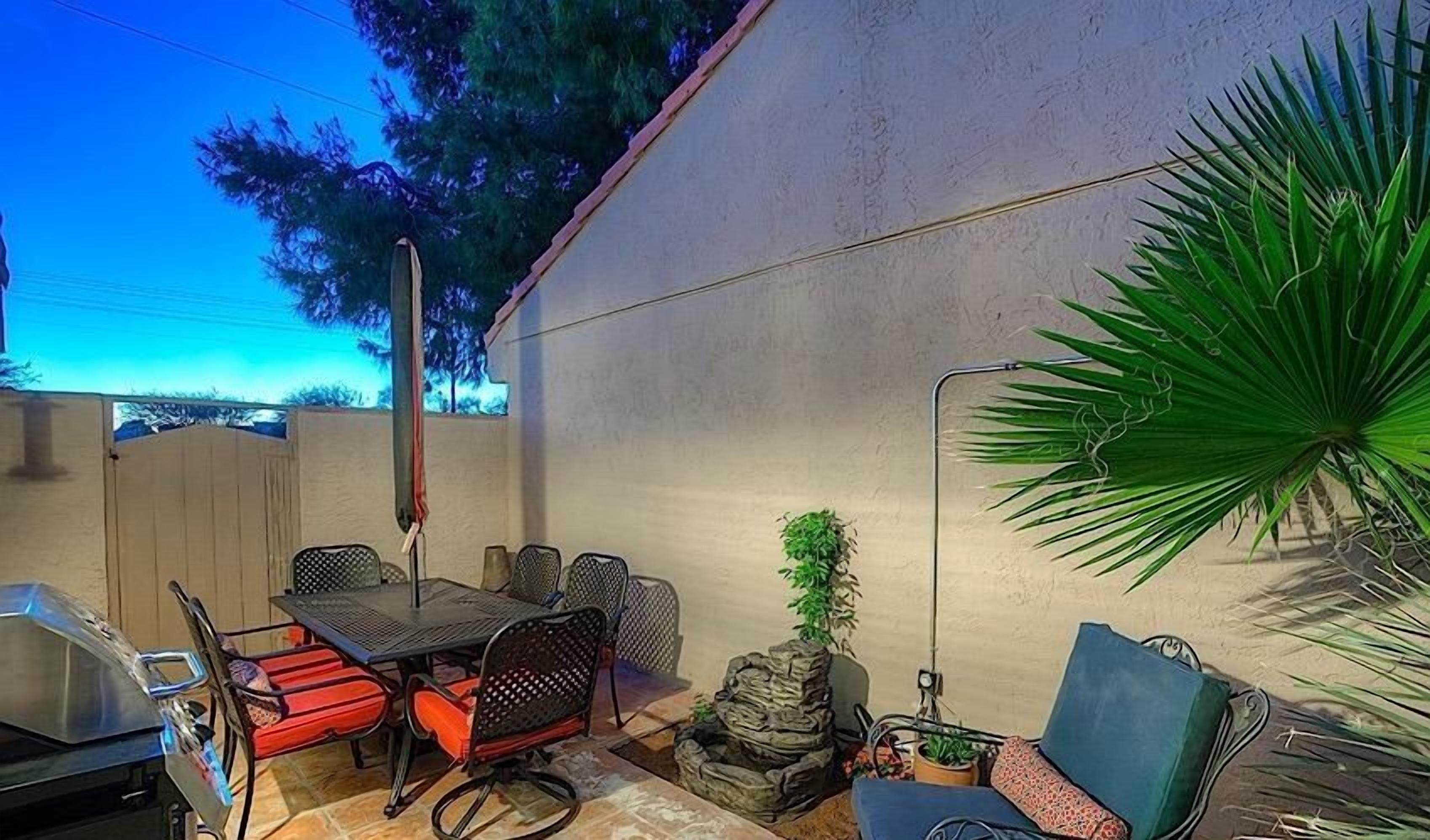 A patio area with a table and chairs, a grill, a potted plant, and a blue sofa.