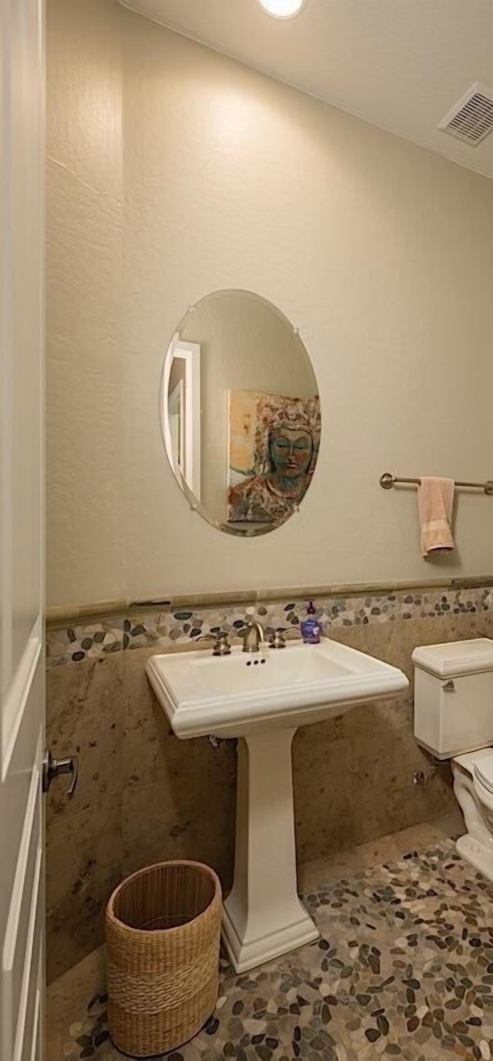 Une salle de bain avec un lavabo blanc, un miroir rond, des toilettes et un sol recouvert de mosaïques.
