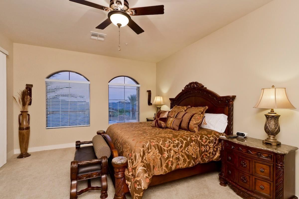A bedroom with a large bed, two bedside lamps, a wooden nightstand, a chair, and a ceiling fan.