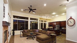 A spacious living room with a sectional sofa, a fireplace, and a kitchen area with wooden cabinets.
