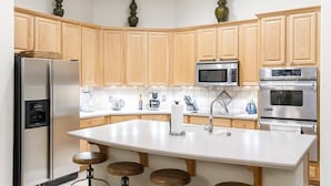 A modern kitchen with wooden cabinets, stainless steel appliances, a central island with stools, and decorative vases. - Sonoran Desert Retreat By Signature Vacation Rentals (Scottsdale)