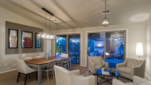 A spacious dining area with a wooden table and white chairs, a seating area with a round coffee table, and a view of a pool through large sliding glass doors. - Sonoran Desert Retreat By Signature Vacation Rentals (Scottsdale)