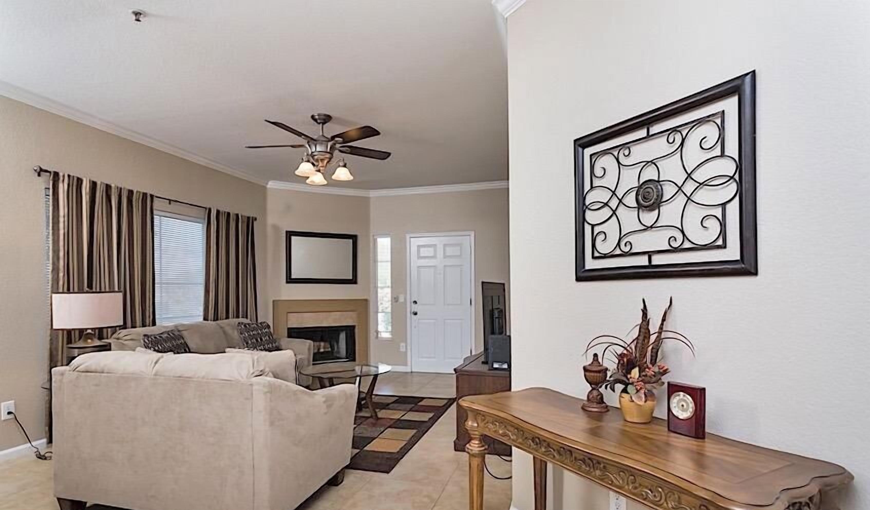 A living room with a beige sofa, a coffee table, a fireplace, and a ceiling fan.