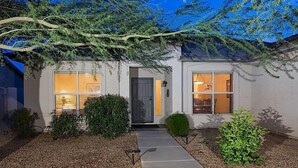 Une maison moderne avec une porte sombre, deux fenêtres équipées de stores et un chemin menant à l'entrée.