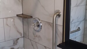 A bathroom with a white sink, a mirror, a shower with a handheld showerhead, and a grab bar. - Travel Inn (Oakland)