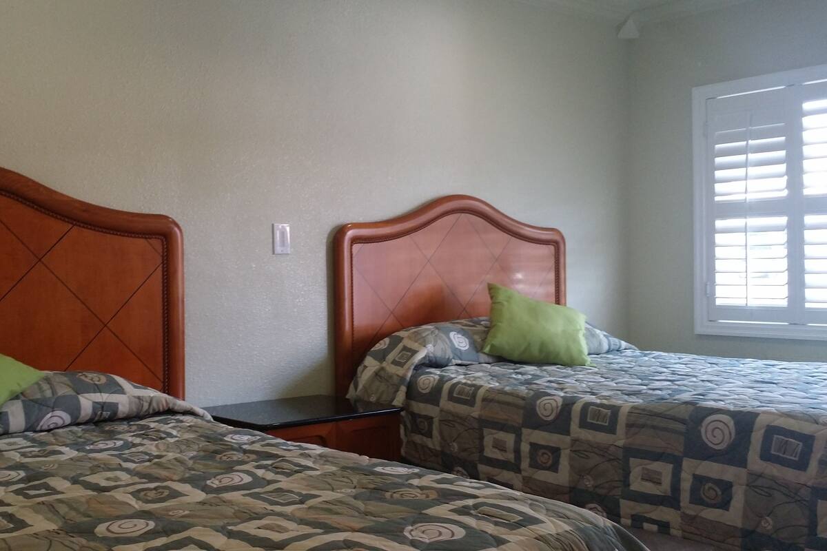 Two single beds with patterned bedding, a wooden headboard, and a window with blinds.